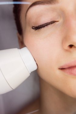 Dermatologist giving facial massage to patient through sonic lifting in clinic